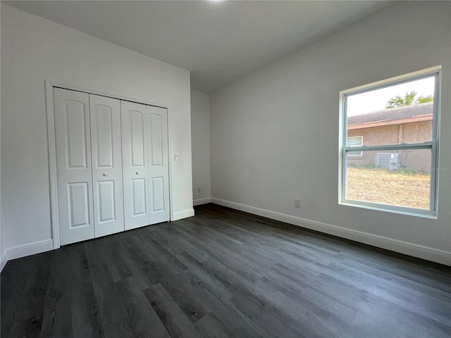 unfurnished bedroom with dark wood finished floors, a closet, and baseboards