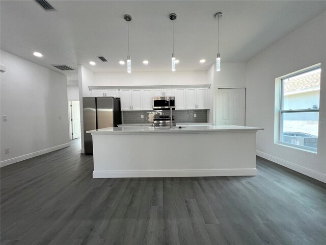 kitchen with visible vents, stainless steel appliances, white cabinets, decorative backsplash, and a large island with sink