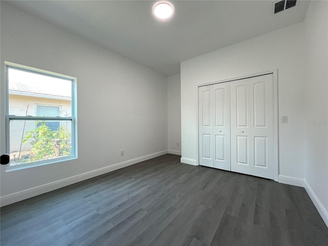 unfurnished bedroom featuring visible vents, baseboards, a closet, and dark wood-style floors