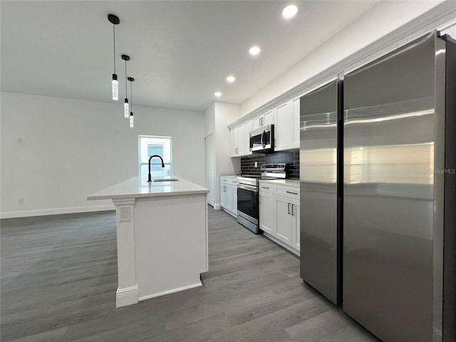 kitchen featuring an island with sink, a sink, backsplash, wood finished floors, and stainless steel appliances