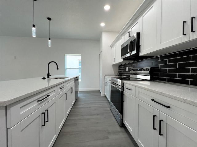 kitchen featuring pendant lighting, a sink, backsplash, white cabinetry, and appliances with stainless steel finishes