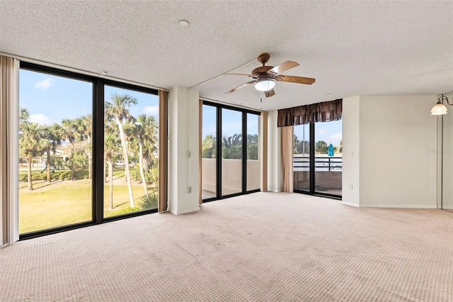 empty room featuring expansive windows, baseboards, ceiling fan, a textured ceiling, and light colored carpet