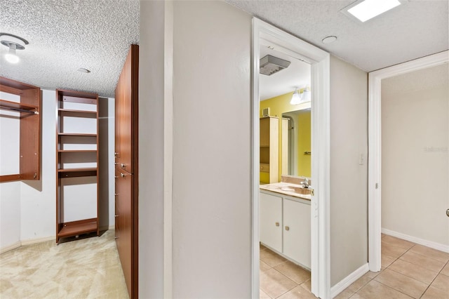 hallway with a sink, baseboards, a textured ceiling, and light tile patterned flooring