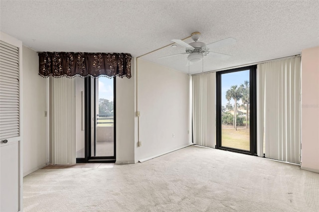 spare room with a textured ceiling, floor to ceiling windows, a ceiling fan, and light carpet