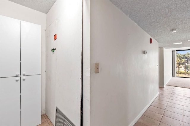 hallway with light tile patterned floors, visible vents, a textured ceiling, and baseboards