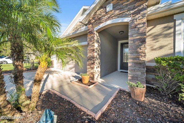 view of exterior entry with stone siding, stucco siding, and an attached garage