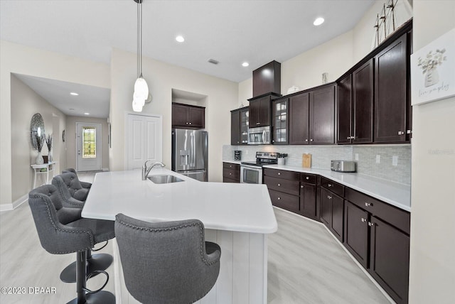 kitchen with a breakfast bar area, a sink, glass insert cabinets, appliances with stainless steel finishes, and tasteful backsplash