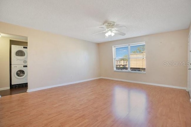 empty room featuring baseboards, stacked washing maching and dryer, wood finished floors, a textured ceiling, and a ceiling fan