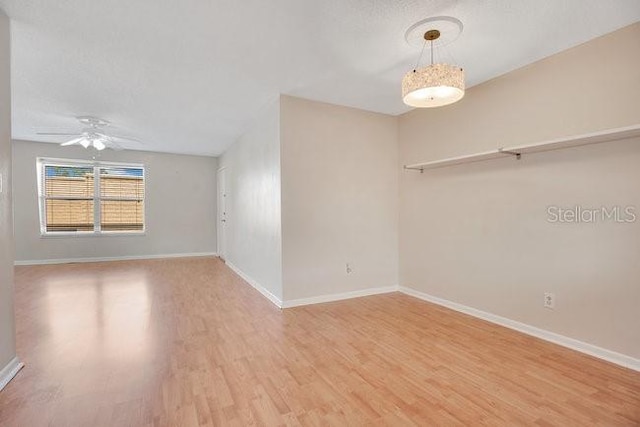 empty room featuring a textured ceiling, wood finished floors, baseboards, and ceiling fan