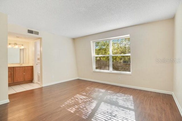 empty room featuring visible vents, baseboards, light wood-type flooring, and a textured ceiling