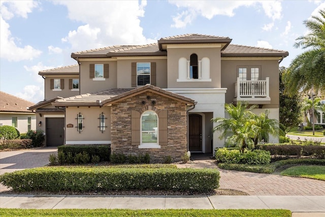 mediterranean / spanish house with a tile roof, decorative driveway, stone siding, and stucco siding