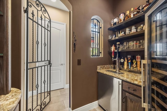 bar with baseboards, arched walkways, wet bar, and light tile patterned flooring