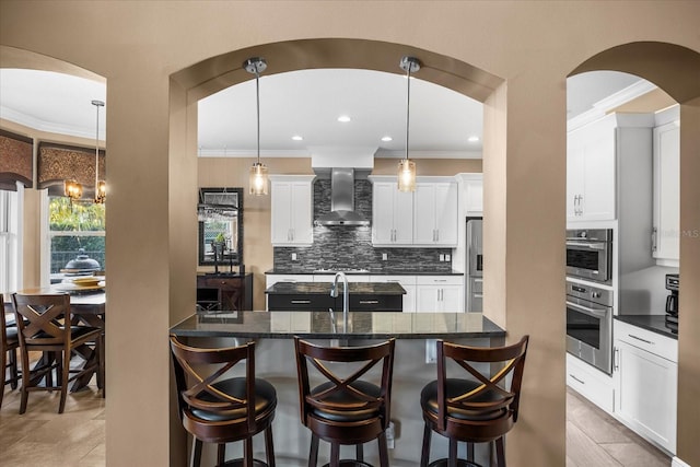 kitchen featuring tasteful backsplash, wall chimney range hood, a breakfast bar area, appliances with stainless steel finishes, and arched walkways