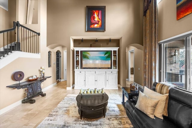 living area featuring baseboards, arched walkways, a high ceiling, and stairs