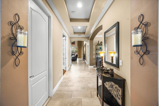 hallway with baseboards, arched walkways, and a raised ceiling