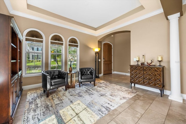 sitting room with arched walkways, ornate columns, baseboards, and a tray ceiling