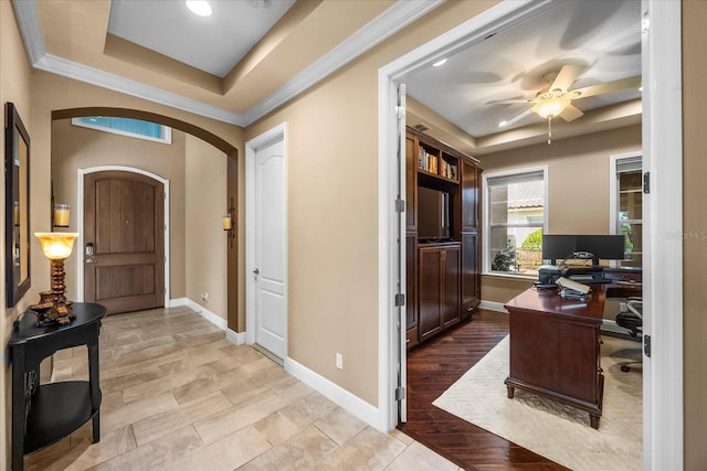 entryway with a tray ceiling, baseboards, arched walkways, and light wood-type flooring