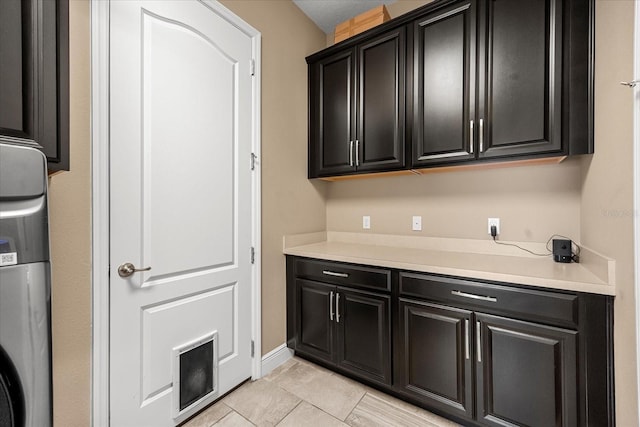 interior space featuring light tile patterned floors, light countertops, dark cabinetry, and baseboards