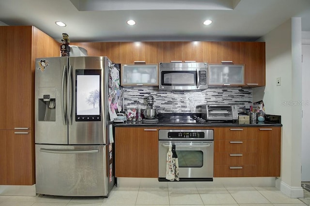 kitchen with brown cabinets, dark countertops, appliances with stainless steel finishes, and tasteful backsplash