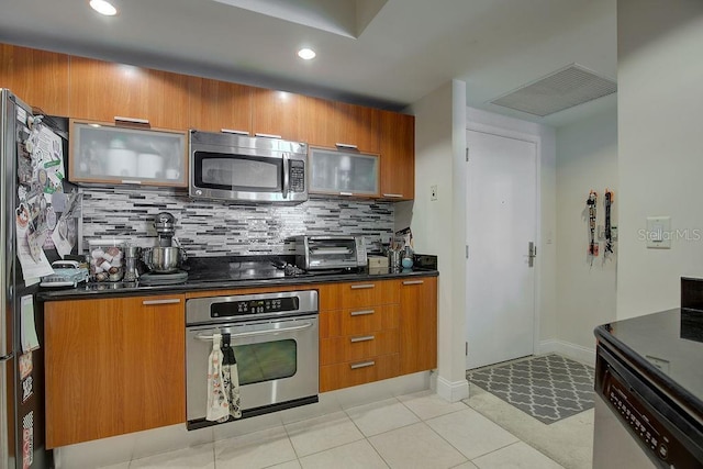 kitchen with brown cabinetry, light tile patterned floors, backsplash, and appliances with stainless steel finishes