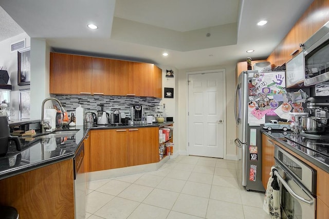 kitchen featuring visible vents, a sink, stainless steel appliances, brown cabinetry, and a raised ceiling