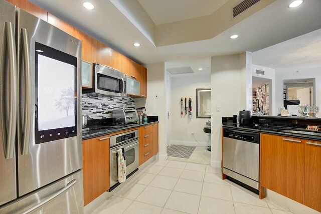 kitchen featuring dark countertops, backsplash, stainless steel appliances, and brown cabinetry