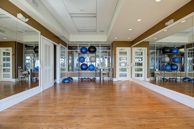 exercise room with visible vents, a tray ceiling, and wood finished floors