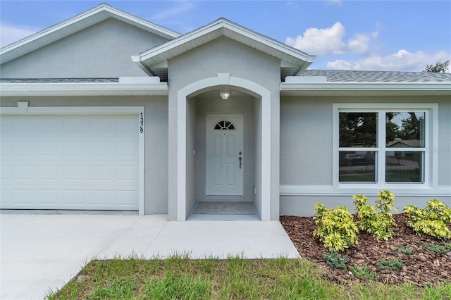 property entrance featuring a shingled roof, an attached garage, and stucco siding