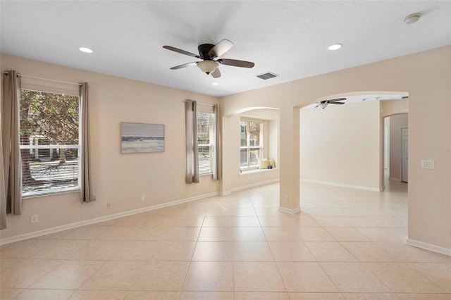 empty room featuring light tile patterned floors, arched walkways, visible vents, and a wealth of natural light