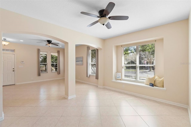 empty room with a wealth of natural light, baseboards, arched walkways, and light tile patterned floors