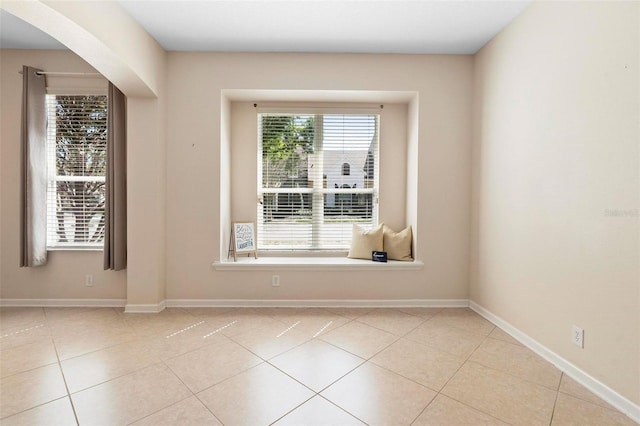 tiled spare room featuring arched walkways and baseboards