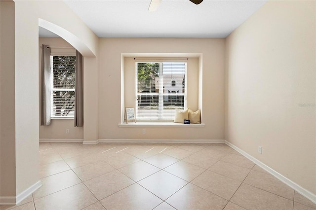 spare room with tile patterned floors, arched walkways, baseboards, and ceiling fan