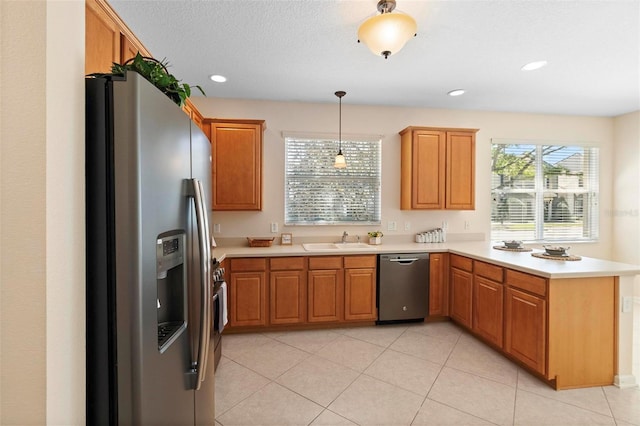 kitchen with a sink, appliances with stainless steel finishes, a peninsula, light countertops, and hanging light fixtures