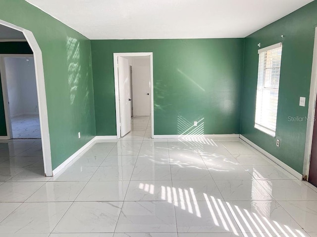 empty room with baseboards, marble finish floor, and arched walkways