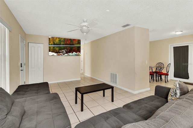 living room featuring light tile patterned floors, visible vents, a textured ceiling, and ceiling fan