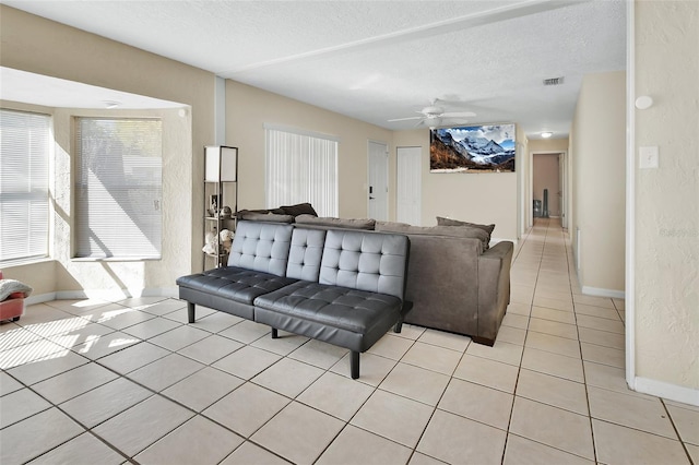 living room with visible vents, baseboards, ceiling fan, light tile patterned flooring, and a textured ceiling