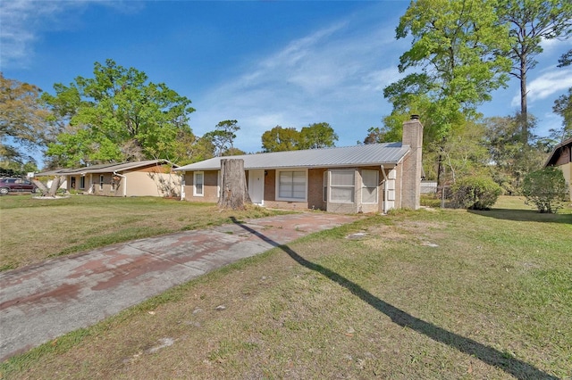 ranch-style house featuring a front yard, a chimney, concrete driveway, brick siding, and metal roof