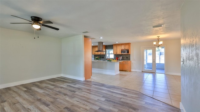 unfurnished living room with ceiling fan with notable chandelier, visible vents, baseboards, and light wood-type flooring