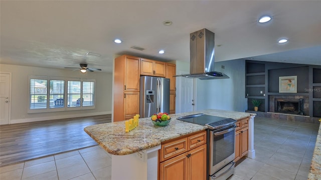 kitchen with built in shelves, a tiled fireplace, open floor plan, stainless steel appliances, and island range hood