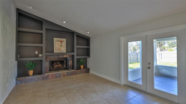 unfurnished living room with a tiled fireplace, built in features, french doors, light tile patterned floors, and vaulted ceiling