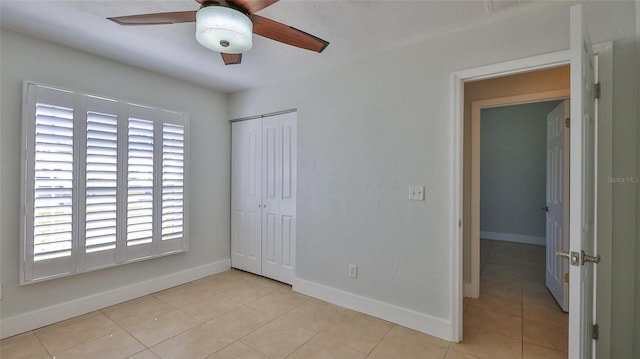 unfurnished bedroom with light tile patterned floors, a closet, baseboards, and a ceiling fan