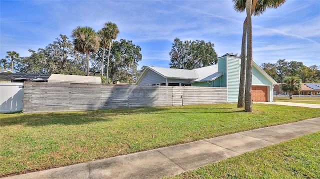 view of side of property with fence private yard, a chimney, driveway, a yard, and an attached garage