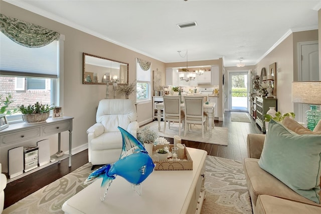 living area with wood finished floors, baseboards, visible vents, ornamental molding, and a chandelier