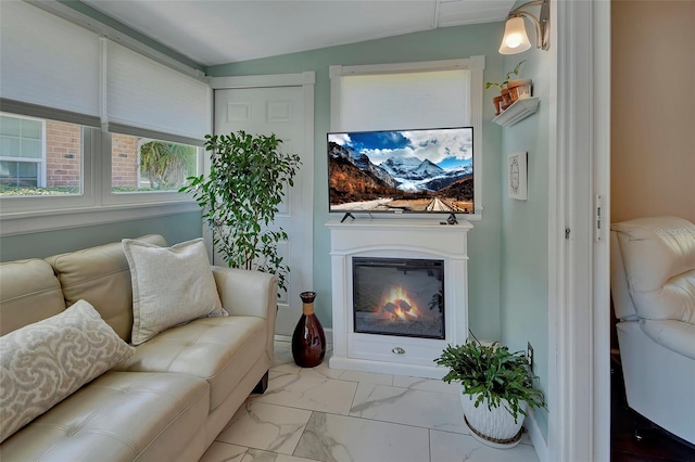 living room featuring a glass covered fireplace, vaulted ceiling, and marble finish floor