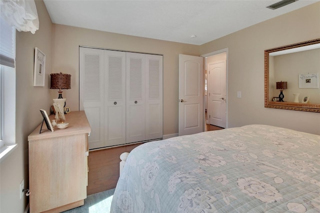 bedroom with wood finished floors, visible vents, and a closet