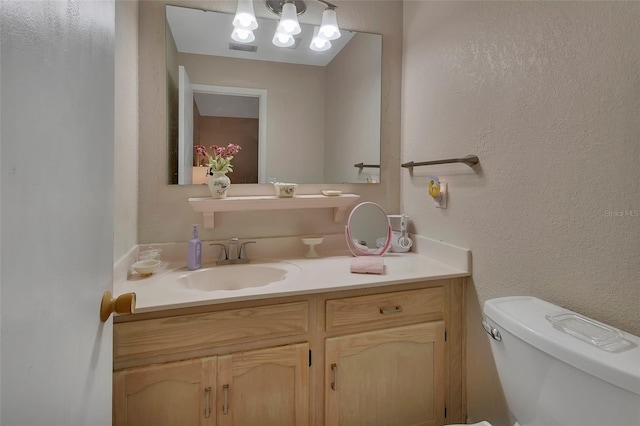 bathroom with visible vents, toilet, vanity, and a textured wall