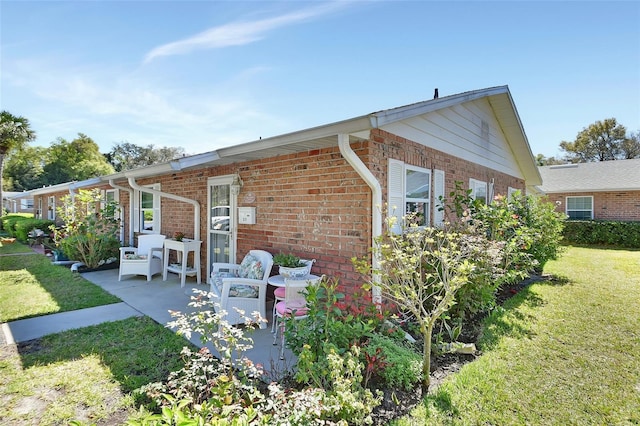 rear view of house featuring brick siding, a patio area, and a lawn