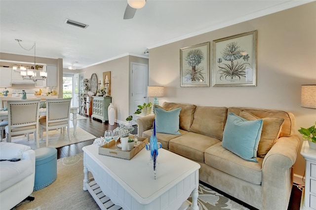 living room with wood finished floors, ceiling fan with notable chandelier, baseboards, ornamental molding, and visible vents