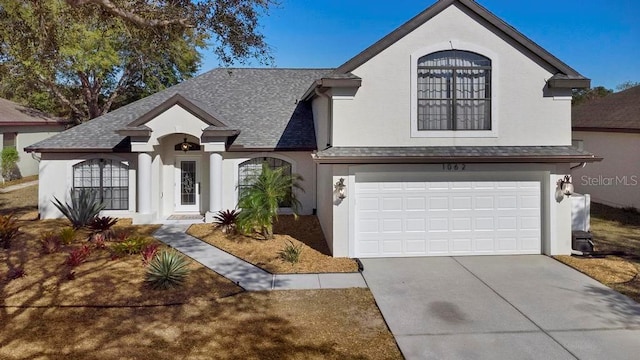 french country inspired facade featuring a shingled roof, a garage, driveway, and stucco siding