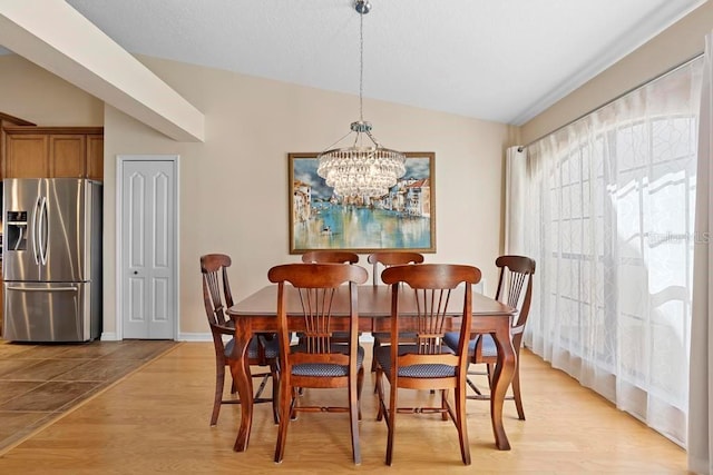 dining space with lofted ceiling, light wood-style flooring, a notable chandelier, and baseboards